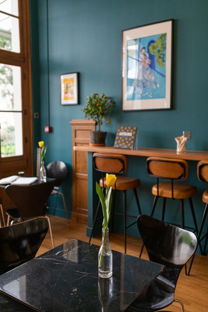 Salle de La Caféothèque Reid Hall : murs bleu canard, tableaux, tabourets et table de marbre